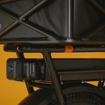 A close up shot of a range extender installed under the rear rack of an ebike that has a basket mounted on it. 